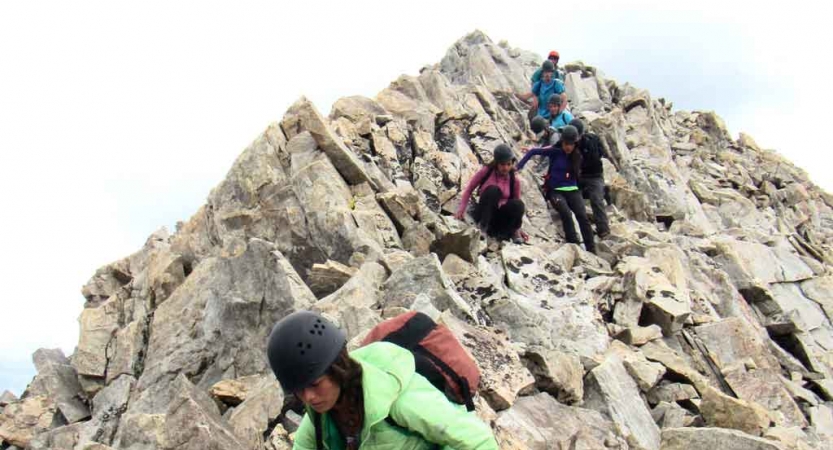 A group of students wearing helmets hike downwards from a rocky incline